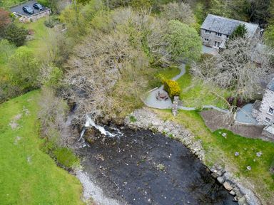 A riverside view with stone houses and outdoor seating area next to water at The Old Water Mill in Kendal
