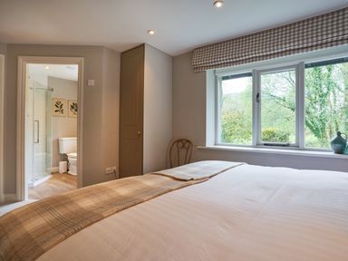A bedroom with a bed and window showing trees outside and an open door to a bathroom at The Old Water Mill in Kendal