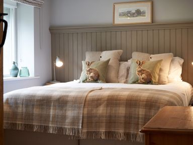 A bedroom with a double bed brown plaid blanket and rabbit print pillows at The Old Water Mill in Kendal