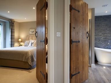 A bedroom with a bed and bedside lamp alongside a bathroom with a freestanding bathtub at The Old Water Mill in Kendal