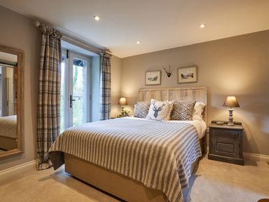 A bedroom with a bed and nightstands with lamps beside glass doors with plaid curtains at The Old Water Mill in Kendal