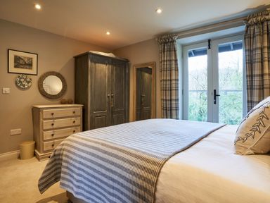 A bedroom with a bed covered by a striped blanket a wooden chest of drawers a dark wooden wardrobe and a full-length mirror at The Old Water Mill in Kendal