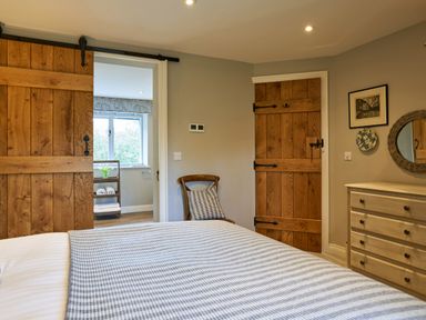 A bedroom with a bed a wooden chair a dresser and a door leading to a bathroom at The Old Water Mill in Kendal