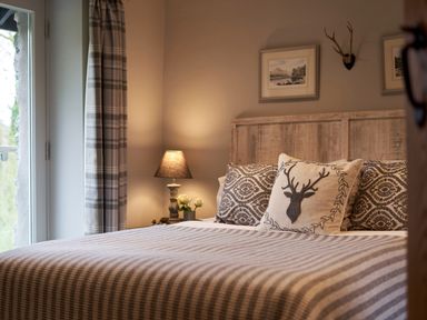 A bedroom with a wooden headboard striped bedspread a lamp and curtains at The Old Water Mill in Kendal