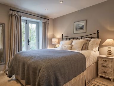 A bedroom with a bed with cushions and blankets two bedside tables with lamps and curtain covered windows at The Old Water Mill in Kendal