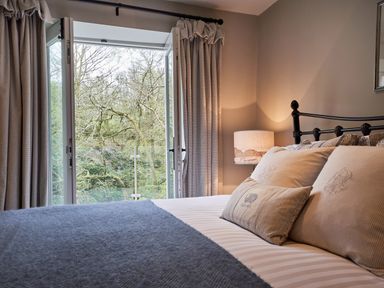 A bedroom with bed pillows lamp and an open window showing trees outside at The Old Water Mill in Kendal