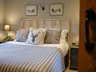 A bedroom with a wooden headboard a bed with patterned pillows and a striped blanket two framed pictures and a mounted deer antler at The Old Water Mill in Kendal