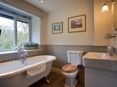 A bathroom with a freestanding bathtub beside a window a toilet with a wooden seat and a sink at The Old Water Mill in Kendal