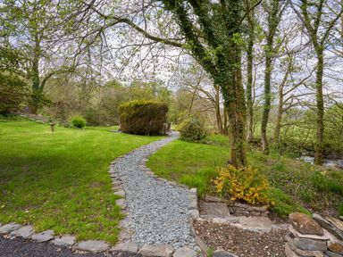 A garden path made of gravel winding through green grass and trees at The Old Water Mill in Kendal