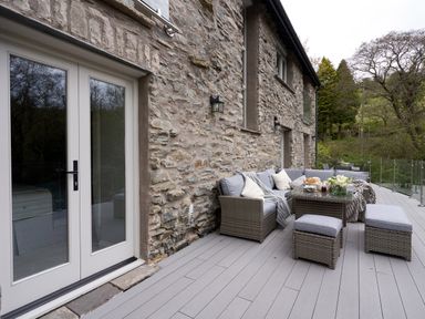 An outdoor patio with wicker furniture and cushions next to a stone wall of a house at The Old Water Mill in Kendal