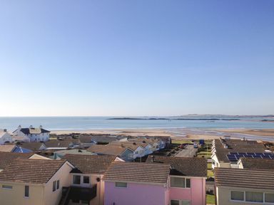 A view of houses with rooftops near a beach and the sea under a clear sky at Sandy Toes in Rhosneigr