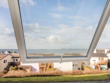 A tilted open window overlooking houses rooftops and the ocean beyond at Sandy Toes in Rhosneigr