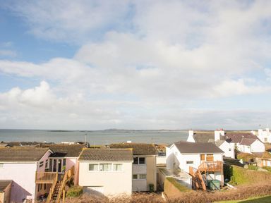 A view of houses overlooking the sea under a partly cloudy sky at Sandy Toes in Rhosneigr
