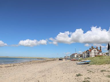A sandy beach with small boats on the shore and houses along the coast at Sandy Toes in Rhosneigr