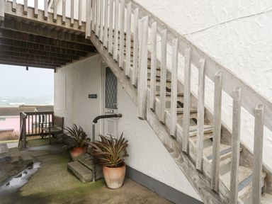 An outdoor stairway with wooden railings next to a white door with potted plants underneath at Sandy Toes in Rhosneigr