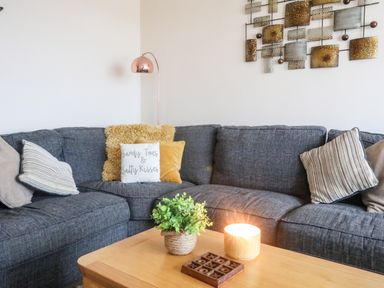 A corner sofa with cushions a coffee table with a plant a lit candle and a tic tac toe game in a living room at Sandy Toes in Rhosneigr