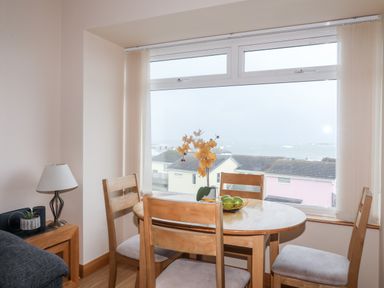 A dining area with round wooden table and four chairs near a window showing rooftops at Sandy Toes in Rhosneigr