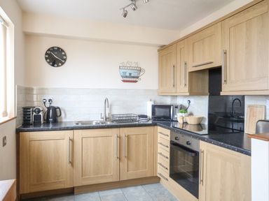 A kitchen with wooden cabinets black countertop a sink microwave kettle and oven at Sandy Toes in Rhosneigr