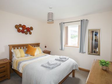 A bedroom with a wooden bed with pillows and folded towels on the bed at Sandy Toes in Rhosneigr