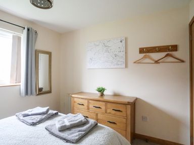 A bedroom with a bed with folded towels a wooden dresser a wall mirror a map on the wall and coat hooks at Sandy Toes in Rhosneigr