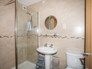 A bathroom with a shower enclosure a pedestal sink with two taps a round mirror and a toilet at Sandy Toes in Rhosneigr