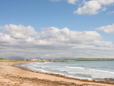 A sandy beach with seaweed and waves near houses and green fields at Sandy Toes in Rhosneigr