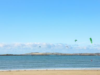 A sandy beach with sea and kite surfers on water at Sandy Toes in Rhosneigr