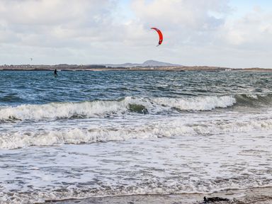 A beach with waves and a person kite surfing in the sea at Sandy Toes in Rhosneigr