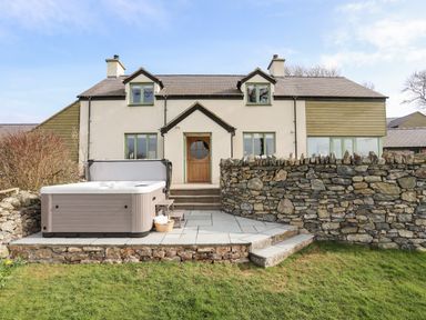 A backyard patio with a hot tub stone wall and a two-story house in the background at Dolwaenydd in Brynsiencyn