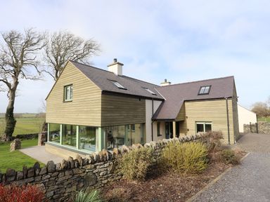 A modern house with stone wall and large windows surrounded by grass and trees at Dolwaenydd in Brynsiencyn