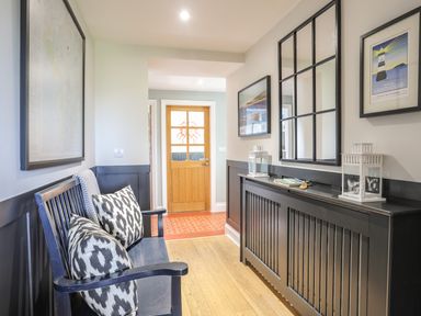 A hallway with a black bench with patterned cushions a wooden floor a black radiator cover with lanterns and framed artwork at Dolwaenydd in Brynsiencyn
