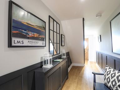 A hallway with wooden floor a black bench a black wall panel and framed pictures at Dolwaenydd in Brynsiencyn