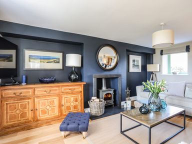 A living room with a wooden cabinet tufted stool coffee table with flowers and a fireplace at Dolwaenydd in Brynsiencyn