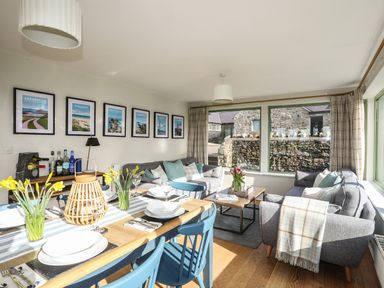 A living and dining room with blue chairs a wooden table and grey sofas at Dolwaenydd in Brynsiencyn