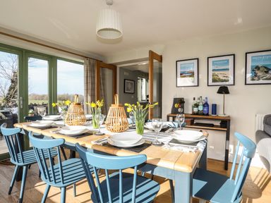 A dining room with a wooden table set with plates glasses yellow flowers and blue chairs at Dolwaenydd in Brynsiencyn