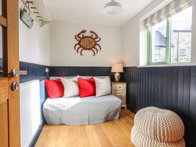 A small room with a sofa with red and white cushions a nightstand with a lamp a knitted pouf and a crab wall decoration at Dolwaenydd Brynsiencyn