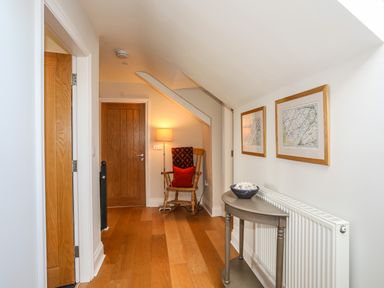 A hallway with wooden floor a wooden rocking chair a table with a bowl and framed pictures on the wall at Dolwaenydd in Brynsiencyn