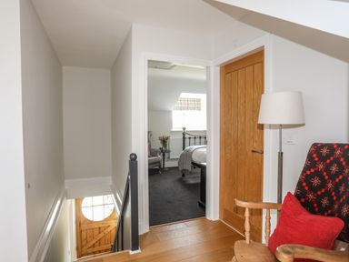 A hallway with wooden floor lamp and chair leading to a bedroom with a bed and armchair at Dolwaenydd in Brynsiencyn