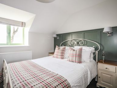 A bedroom with a white metal bed frame polka dot pillows and blanket green paneled wall and a window at Dolwaenydd in Brynsiencyn