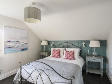 A bedroom with a double metal bed with gray quilt and red pillows two bedside tables with lamps and a painting on the wall at Dolwaenydd in Brynsiencyn