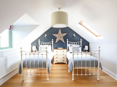 A bedroom with two white beds a wooden floor and slanted ceiling at Dolwaenydd in Brynsiencyn