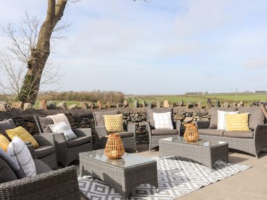 An outdoor seating area with wicker sofas and chairs with cushions a stone wall and fields in the background at Dolwaenydd in Brynsiencyn
