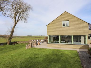 A house with wooden siding and large windows overlooking a grassy lawn and countryside at Dolwaenydd in Brynsiencyn