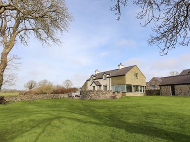 A house with a stone wall and large grassy lawn with leafless trees at Dolwaenydd in Brynsiencyn