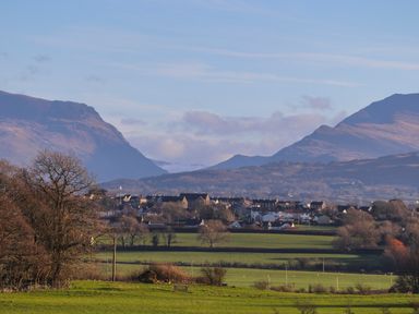 A rural landscape with green fields trees and a small town with mountains in the background at Dolwaenydd in Brynsiencyn