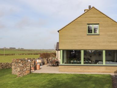 A patio area with outdoor furniture and stone wall next to a wooden house with large windows at Dolwaenydd in Brynsiencyn