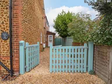 A gravel driveway with a light blue wooden gate leading to a door on a stone and brick house at Job's Cottage in Snettisham