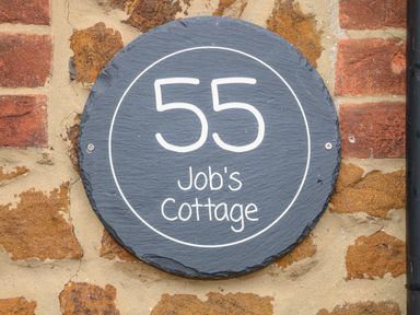 A round house number plaque with the number 55 and the name Jobs Cottage on a brick wall at Jobs Cottage in Snettisham