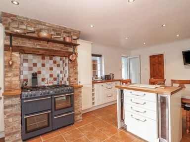 A kitchen with a black stove set in a brick alcove and white cabinetry with a central island at Job's Cottage in Snettisham