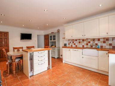 A kitchen with tiled floor wooden countertops and white cabinets dining table with chairs and a wall-mounted TV at Jobs Cottage in Snettisham